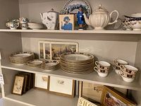 Shelf display showing multiple pieces of Royal Crown Derby Derby Border dinnerware and three Sigmund Samuel winter scene placemats