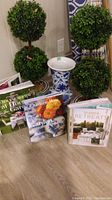 Photo showing two faux topiary plants in ceramic planters, blue and white vase, and three gardening books.
