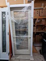 Steel entry door in white frame, wrapped in plastic, showing full glass panel