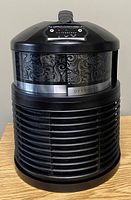 Front view of the black cylindrical Filter Queen Defender air cleaner showing patterned band and control panel on top.