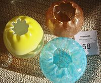 Top view of the three hand blown glass rosebowls placed on a textured surface showing yellow, blue opal, and gold bowls with scalloped openings