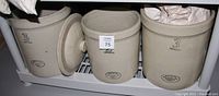Three pottery pickling crocks arranged together, showing two 3-gallon crocks and one 2-gallon crock, all marked '3 Imperial' with one lid beside the crocks.
