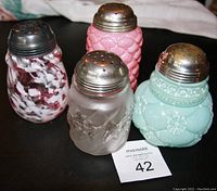 Four antique glass sugar shakers shown together with visible metal tops and intricate glass patterns.