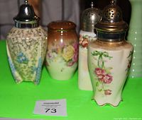 Four antique sugar shakers arranged on a green background, displaying their shapes and floral decorations.