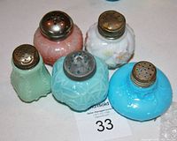 Top view of 5 antique opaque glass shakers with metal tops showing wear and rim nibbles