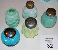 Five antique opaque glass salt shakers of different colors, seen from above showing metal screw lids and one missing lid.