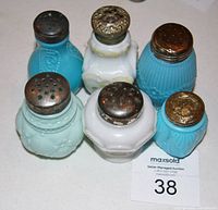 Top-down view of six antique glass shakers showing various opaque colors and metal tops with wear
