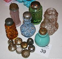 Overview of all six antique glass shakers with several spare metal lids displayed together on a white surface.
