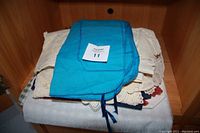 Stack of antique and modern table linens showing a blue silverware storage bag on top and various white and cream colored linens with lace edges underneath