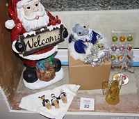 18-inch Santa statue holding "Welcome" sign, Christmas mouse figurine on a box, tiny shiny decorated tree with small colorful ornaments, angel tree-topper, and small decorative items on the surface.