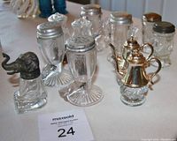 Overview of collectible Victorian glass shakers variety including elephant, human faces, teapots, and other forms, showing metal tops and clear glass bases.