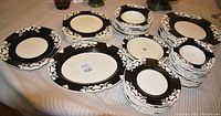 Full view of all china items laid out on a table, showing the black and off-white floral patterned dinnerware including plates and platters.