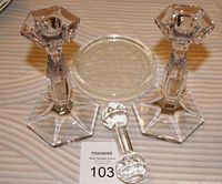 Two Heisey crystal candlesticks with hexagonal bases, round glass knife rest, faceted glass stopper, and wine stand shown from front view on wooden surface.