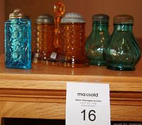 Photo showing five salt shakers: amber hobnail pair on matching stand, two pairs of clear glass salts in blue and green glass patterns.