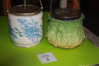 Pair of biscuit barrels, one majolica green cabbage style and one white floral blue ceramic, both with metal lids.