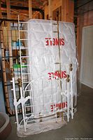 Reproduction iron daybed components leaning against a wall with new mattress behind them, showing white enamel frame and brass finials