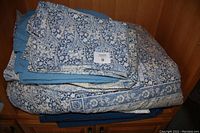 Folded bedding including duvet cover, pillowcases, bed skirt with floral blue and white pattern and blue solid pillowcases.