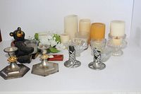 Wide view showing multiple candles, glass and pewter candle holders, and black bear figurine holding one candle