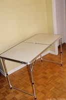 Folding table set up with metal legs extended, laminate surface on display, showing full length and width.