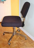 Black office chair with padded fabric seat and backrest, metal base with five legs and casters, angled side view.