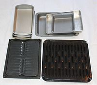 Photo showing seven roasting and baking pans arranged with silver metal pans on top and black enameled pans with ridged surfaces below.
