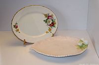 Two china serving trays: an oval floral gold-trimmed Royal Swan tray and a pale pink leaf-shaped serving tray with leaf decoration.