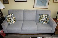 Front view of three-seat light grey fabric sofa with two geometric-pattern accent pillows