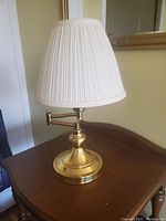 Table lamp with brass swivel neck and pleated white fabric shade on a wooden surface