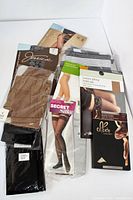 Photo of six different sealed packages of tights and pantyhose laid out on white surface showing brand names and packaging.