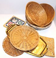 Six serving items including a rectangular gold-tone metal tray with handles and five different woven wicker baskets and trays arranged on a white surface.