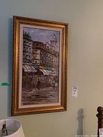 Framed acrylic painting depicting an urban city street scene with buildings and people, in a gold decorative frame