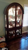 Full view of curio cabinet showing wood finish, arched glass doors, and interior lit glass shelves with displayed items.