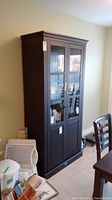 Image showing the front view of the tall, dark brown faux wood cabinet with glass doors revealing shelves inside.