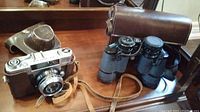 Photo showing Walz Envoy M-35 camera in brown leather case with Bushnell binoculars on wooden surface.
