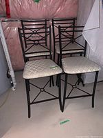 Four matching metal frame bar chairs with fabric seats arranged in a corner, showing their overall shape and design.