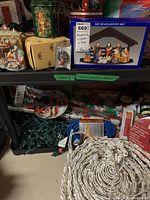Overall view of shelves with boxed nativity set, tins, ornaments, lights, wrapping paper, and cords.