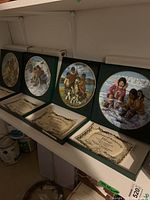 Four Woodridge collector plates in frames displayed on shelf with their certificates of authenticity and boxes.