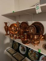 Copper finish plates, pitchers, bowl, mugs, and piggy bank container arranged on a white shelf