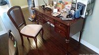 Full view of wooden desk with 5 drawers and wooden chair with upholstered seat and cane back, showing condition and style