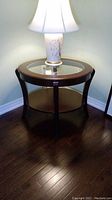 Front view of the round wood end table with lamp on top showing glass inset and lower shelf.