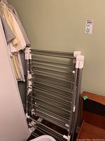 Metal folding clothes drying rack leaning against wall next to clothes closet