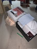 Photo showing packaged Beauty Sleep mattress pad and comforter, folded twin sheet set with light blue and white stripes, piled items including mattress protectors