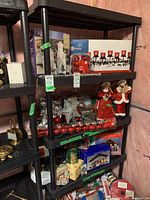 Photo showing black plastic shelving unit with five shelves, containing various holiday decorations and boxes. Shelving unit is the main subject and in good condition.
