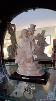 Porcelain bride and groom statuette on stepped wooden base with plaque, showing detailed facial features and wedding attire.
