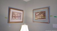 Two framed prints mounted on wall, one depicting a cottage and the other an outdoor scene with two girls with parasols.