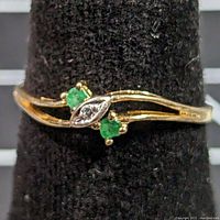 Front view showing two round emeralds flanking a marquise diamond set in white gold bezel