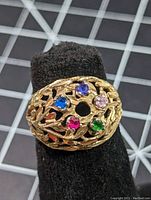 Front view of 14K yellow gold filigree cocktail ring showing five colored gemstones in a circular pattern on a black display.