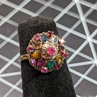Ring front profile showing cluster of various gemstones with different colors and cuts in yellow gold setting.