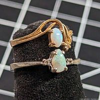 Two 10K opal and diamond rings on black display. One yellow gold ring with oval opal and small diamonds, one white gold ring with pear-shaped opal and small diamonds, showing overall condition and design details.