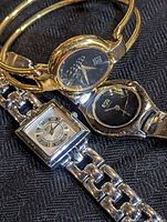 Three ladies wristwatches by ESQ Movado arranged on black fabric background.